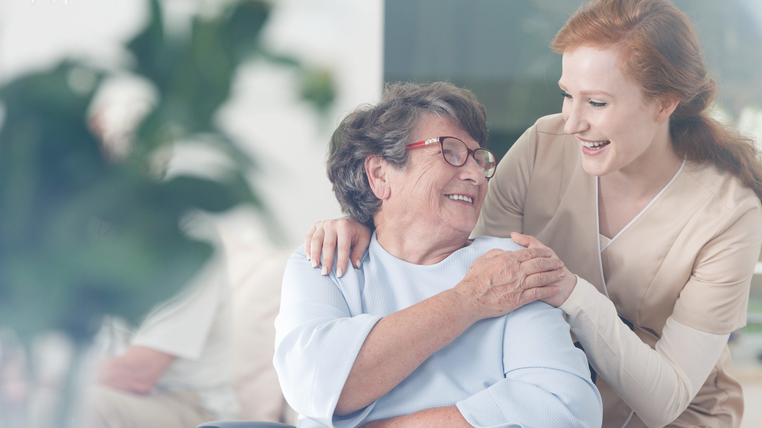 A lady nurse and her patient, an older woman laughing together while holding hands.