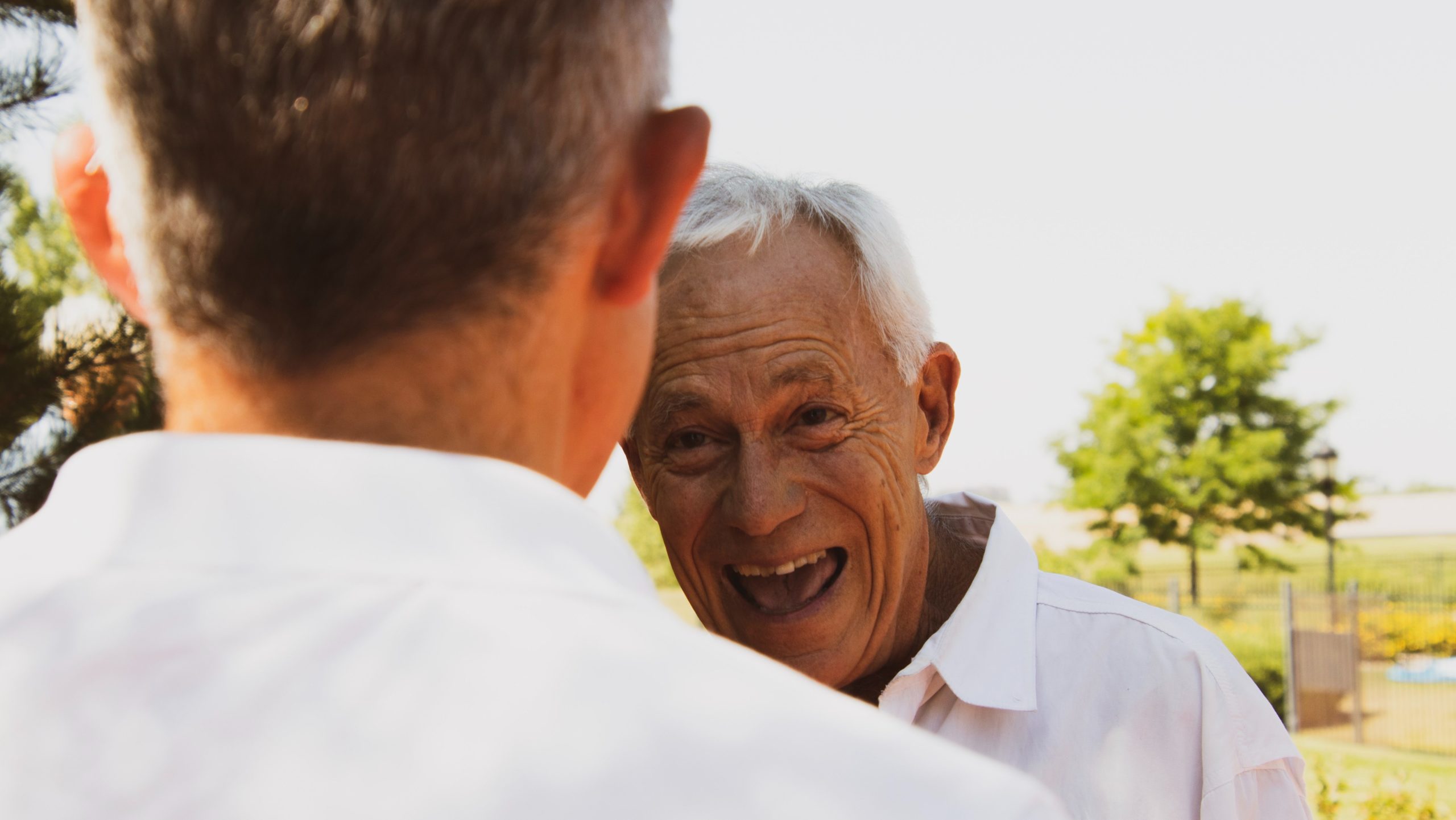 Old man laughing with another man while outside.