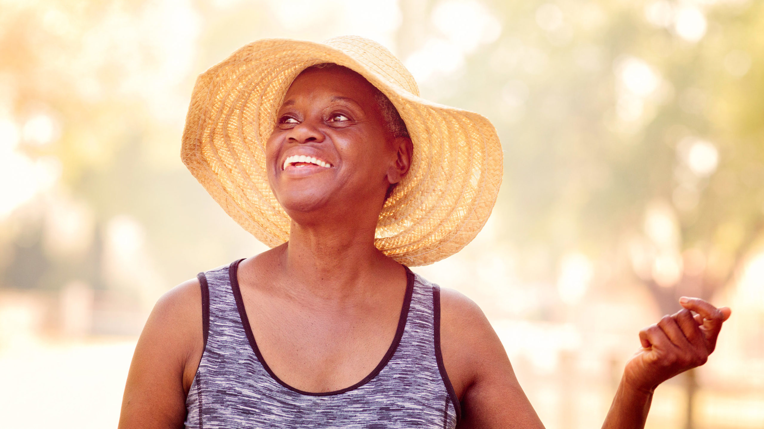 Woman in tank top and sun hat smiling outside.
